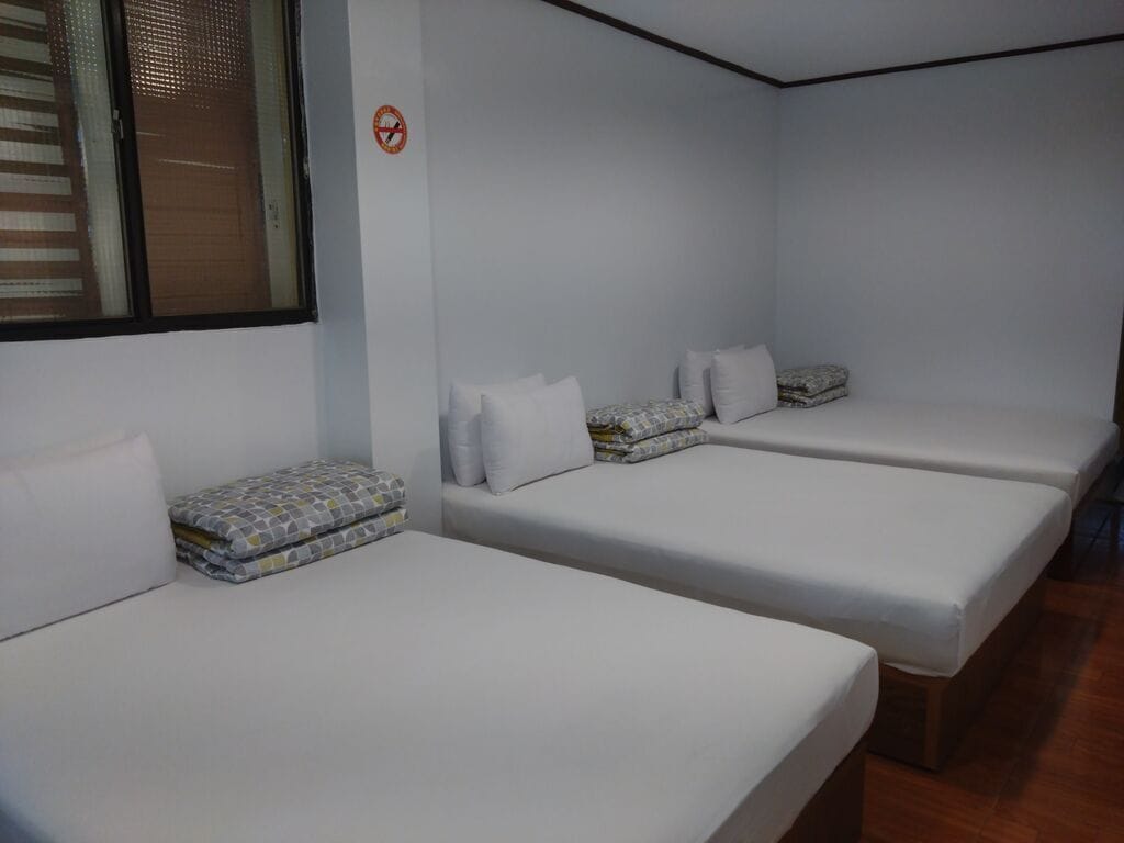 Habitación con tres camas individuales, cada una con almohada y manta doblada.