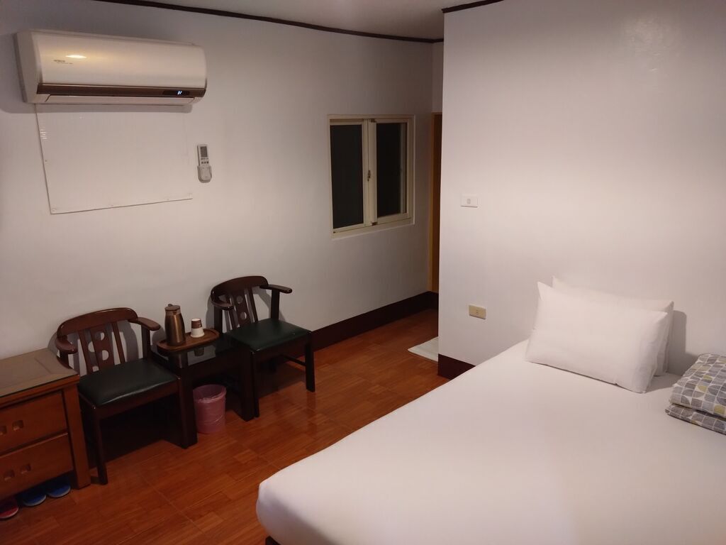 Une pièce comprenant un lit, un bureau avec une chaise, une petite table avec une chaise, une fenêtre et un appareil de climatisation.