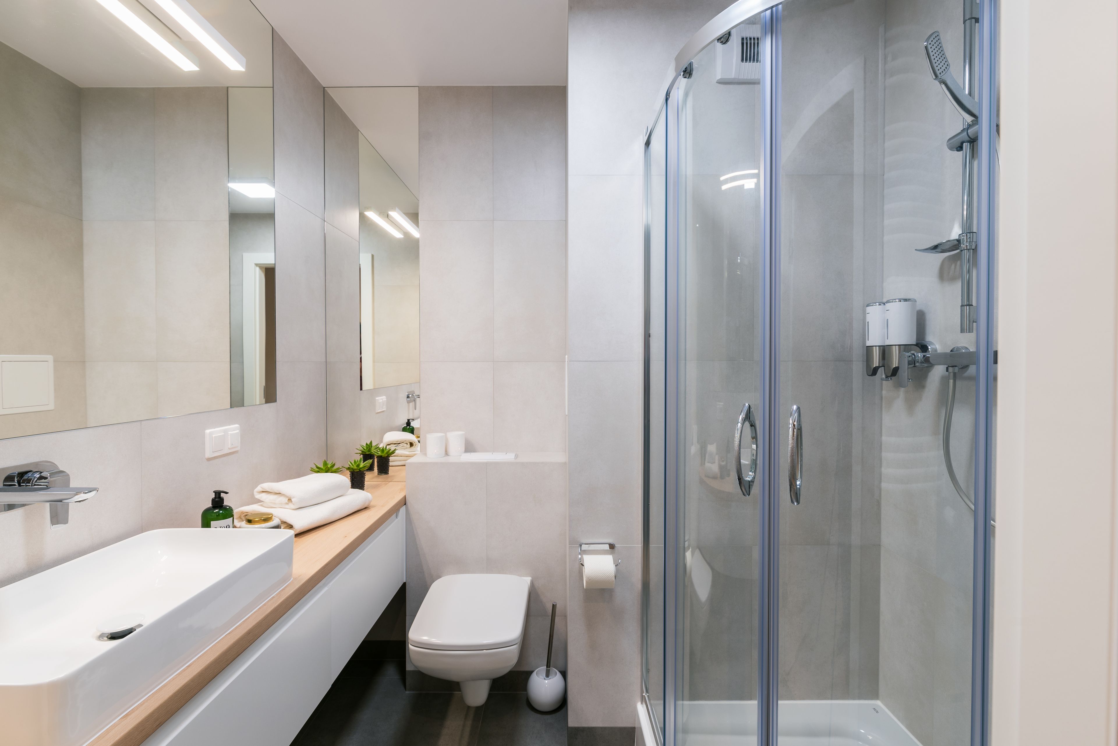 Un baño moderno con ducha de vidrio, un espejo grande y tocador con lavamanos y perchero para toallas.