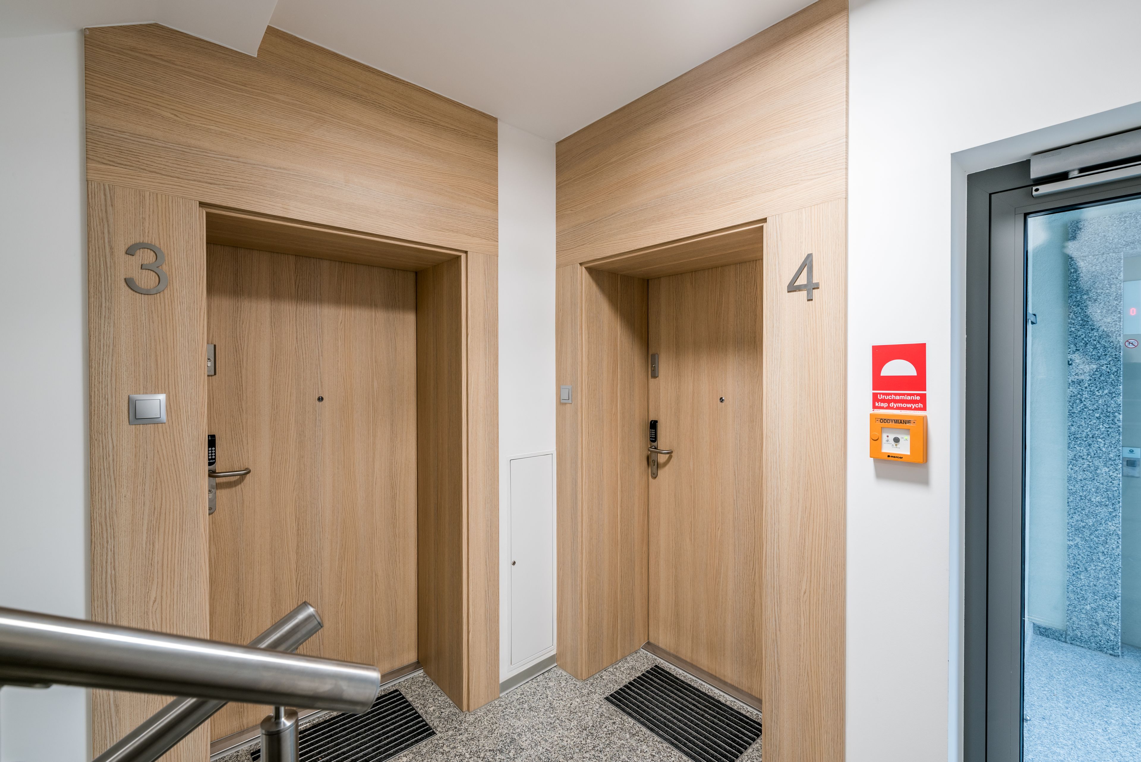 Two wooden doors with numbers 3 and 4, a metal handrail, and a glass door with a red sign.