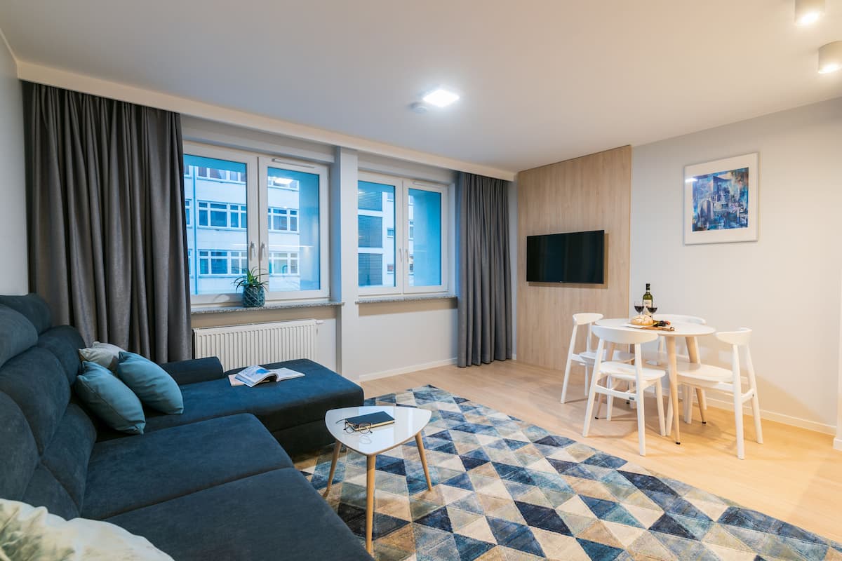 Un salon moderne avec un canapé, une petite table, un coin repas avec des chaises et un téléviseur fixé au mur.