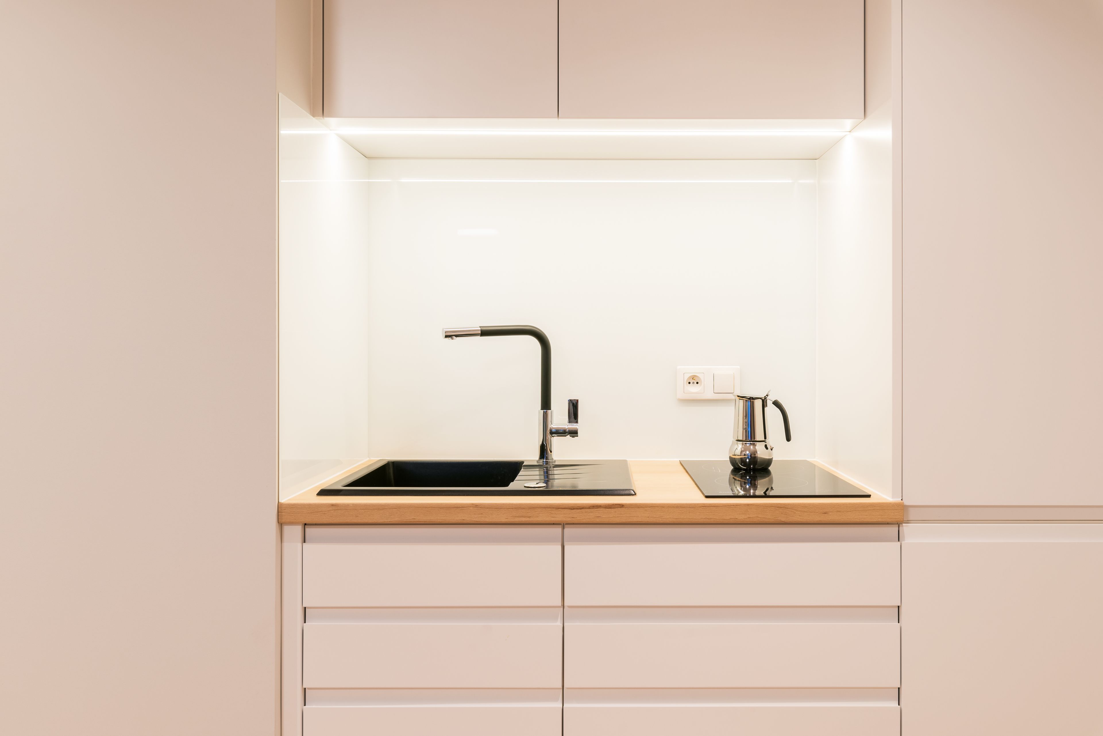 Una cocina moderna con un grifo negro, encimera de madera y armarios blancos.