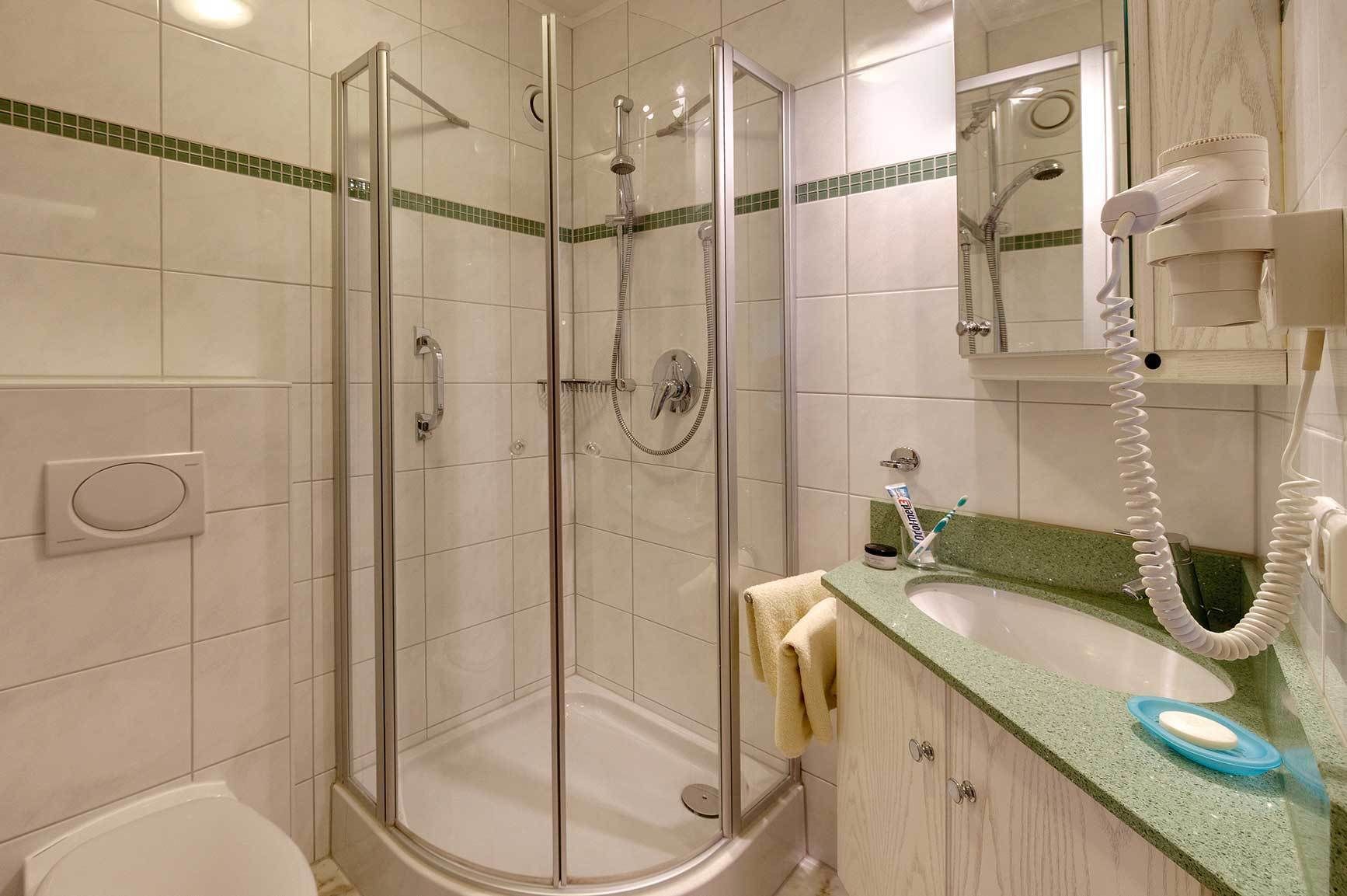 A hotel bathroom with a glass-enclosed shower, a sink with a green countertop, and a mirror with a hairdryer.