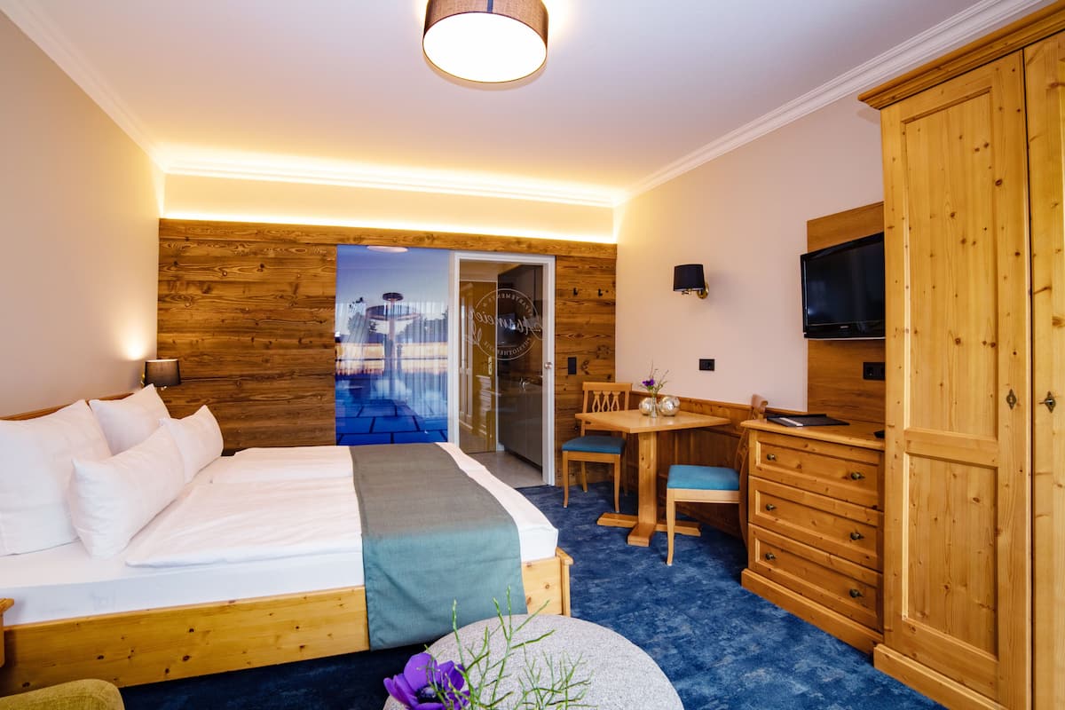 A hotel room with a wooden bed, a desk with a chair, a television, and a wardrobe.