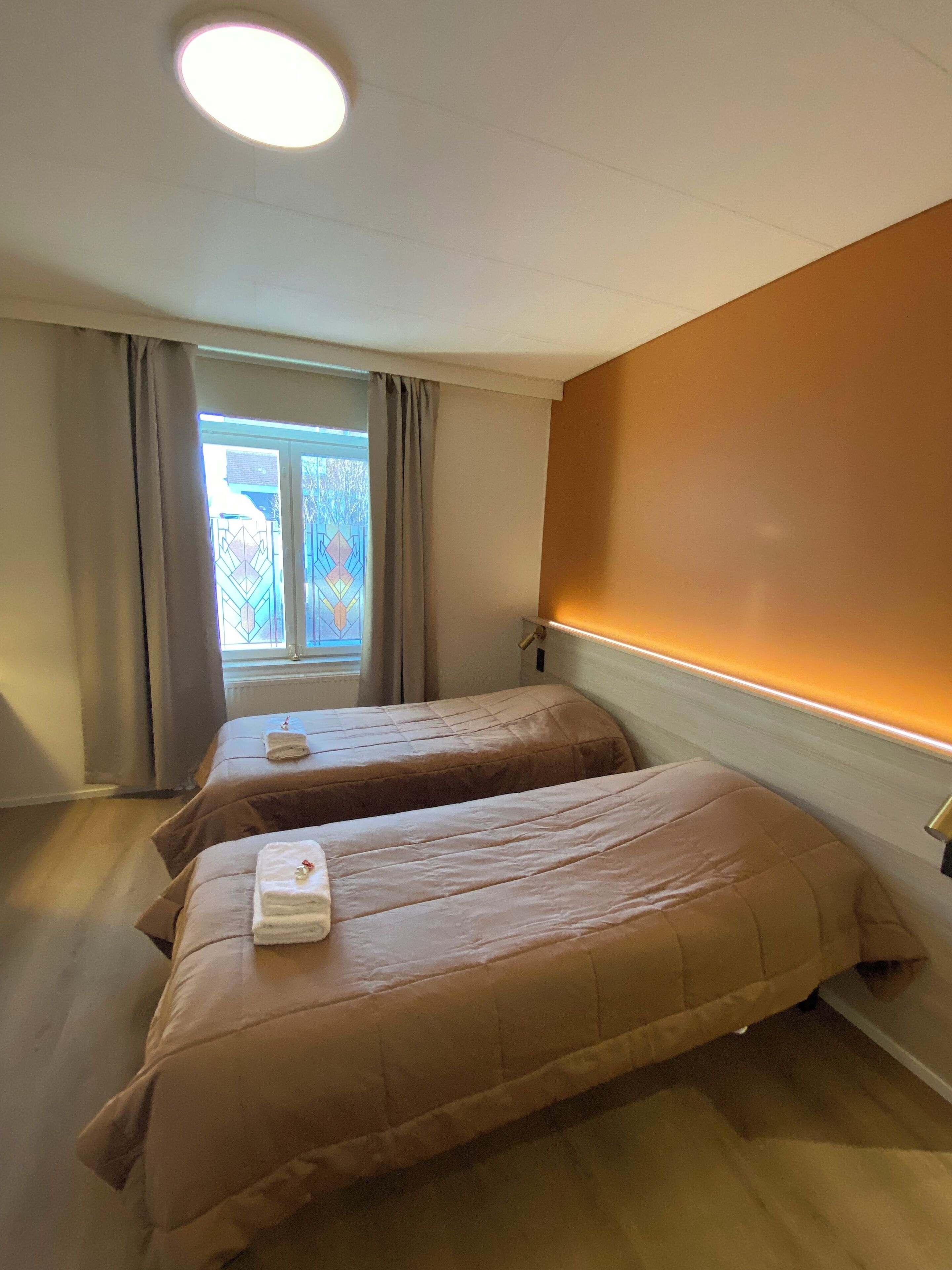 Una habitación con dos camas, una ventana con cortinas y una pared cálida.