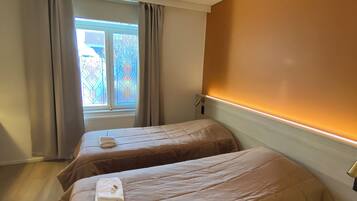 Una habitación con dos camas, una ventana con cortinas y una pared cálida.