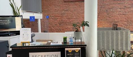 A reception desk with a sign labeled "RECEPTION," a computer monitor, a plant, and a window with a view of the outside.
