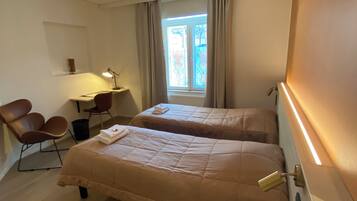 Habitación de hotel con dos camas, un escritorio con lámpara, una silla y una ventana con cortinas.