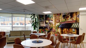 Un espace repas avec des tables et des chaises rondes, un canapé et une fresque murale représentant une scène de rue.