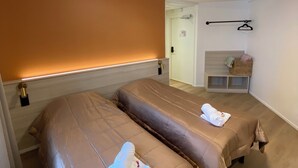 Une chambre d’hôtel avec deux lits, un petit coin salon et une porte donnant accès à la salle de bain.