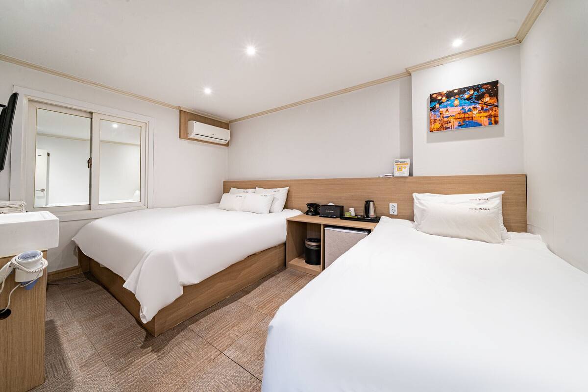A hotel room with two beds, a small desk, a mirror, and an air conditioning unit.