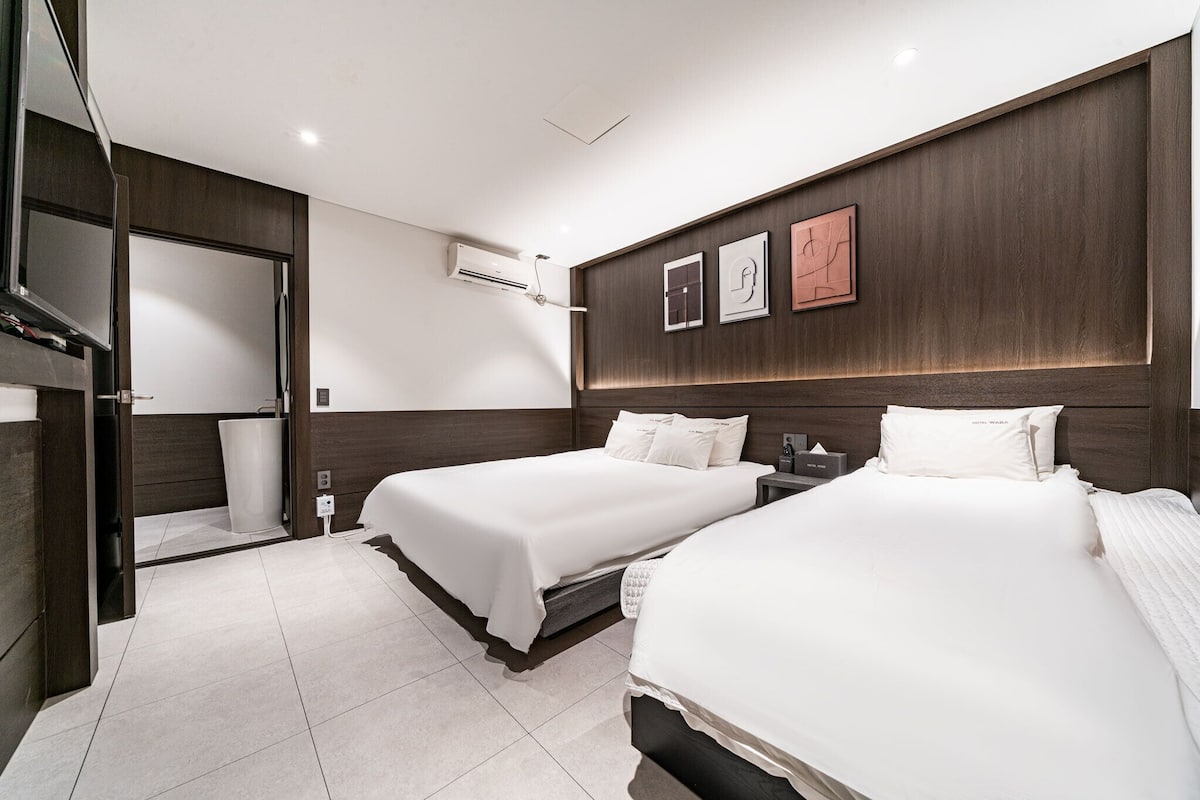 A modern hotel room with two beds, a large mirror, and a wall-mounted air conditioning unit.