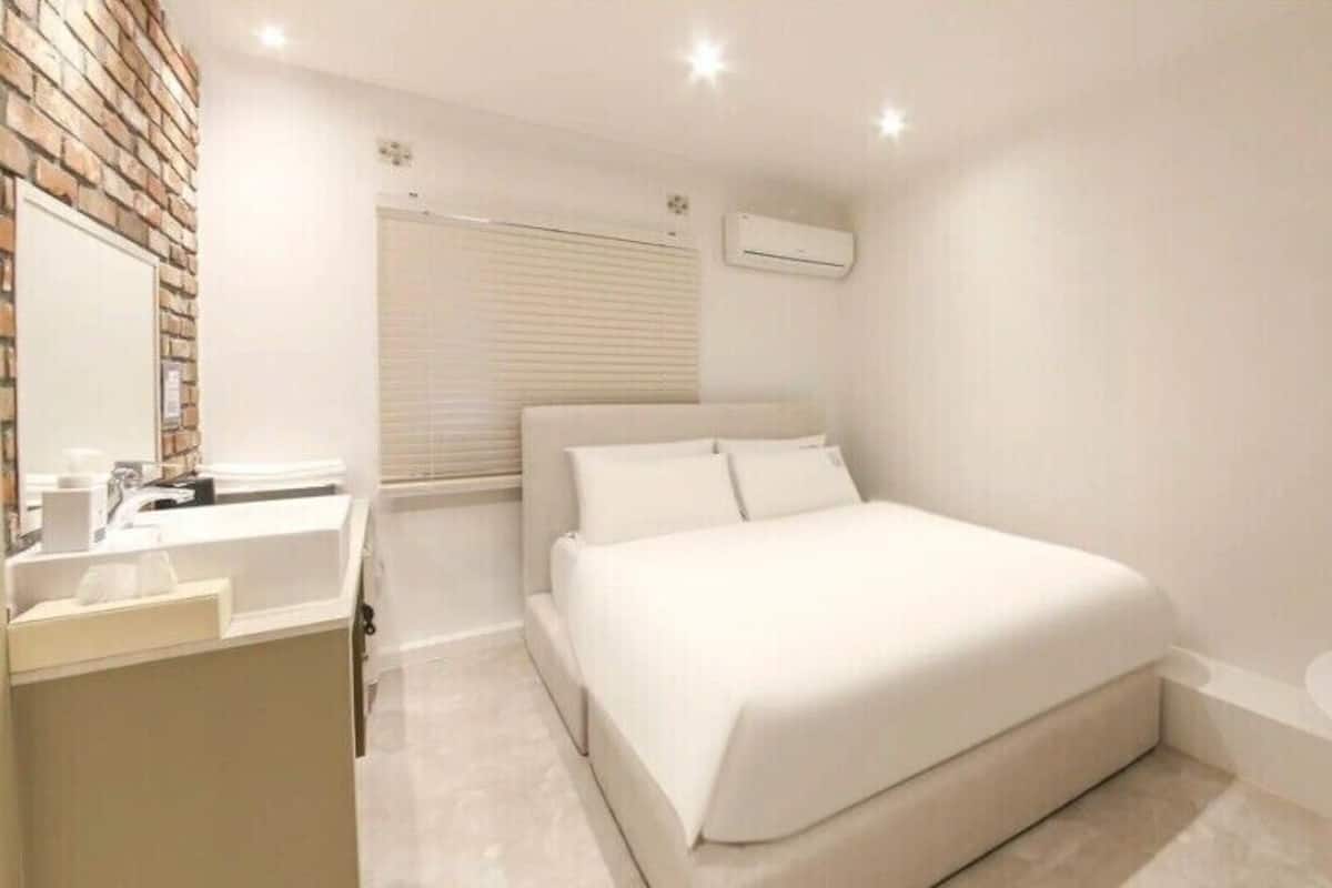A hotel room with a bed, a small table, a sink, and a mirror.