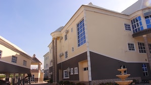 A multi-story building with a beige facade, large windows, and a central fountain.