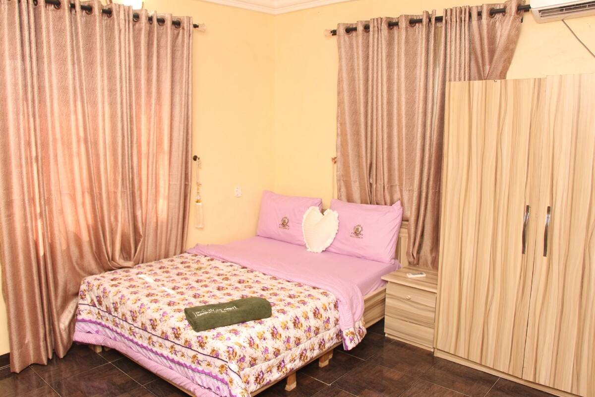 A bedroom with a bed, curtains, a wardrobe, and a nightstand.