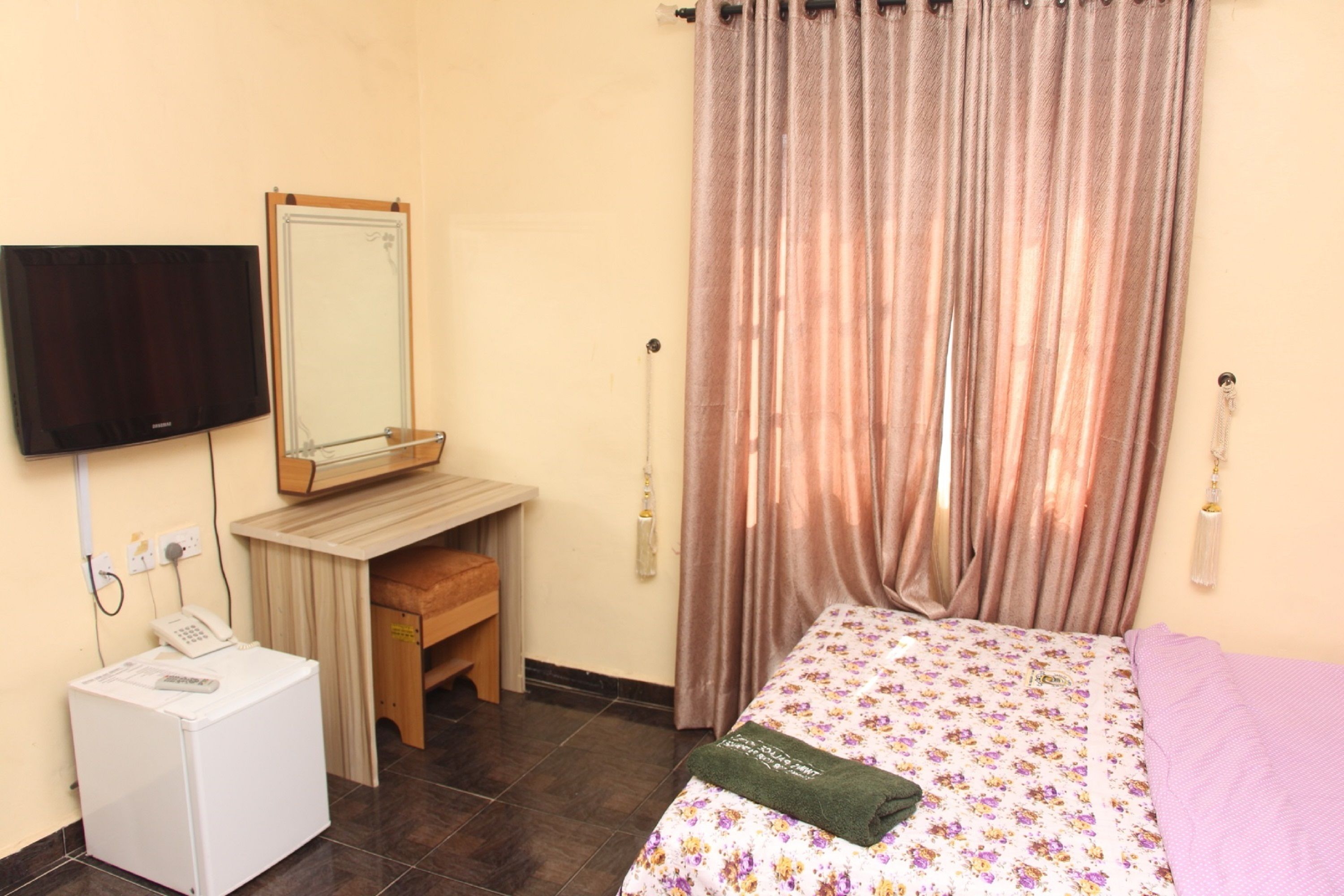 Quarto com cama, escrivaninha, espelho, televisão e máquina de lavar.