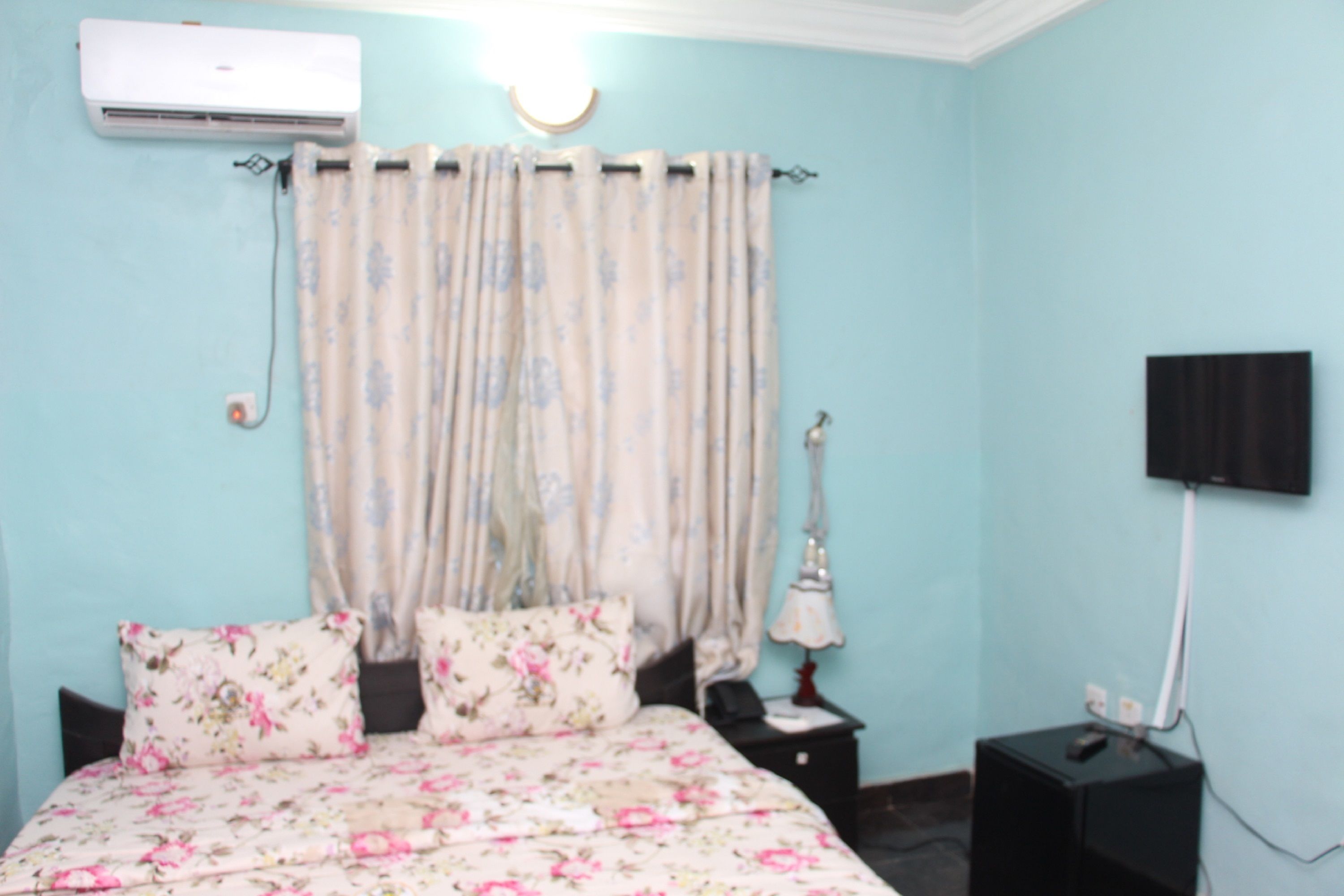 A bedroom with a bed, a nightstand, a lamp, an air conditioner, and a television.