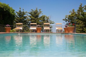 En pool med sex solstolar och två stora terrakotta-krukor med blommor.