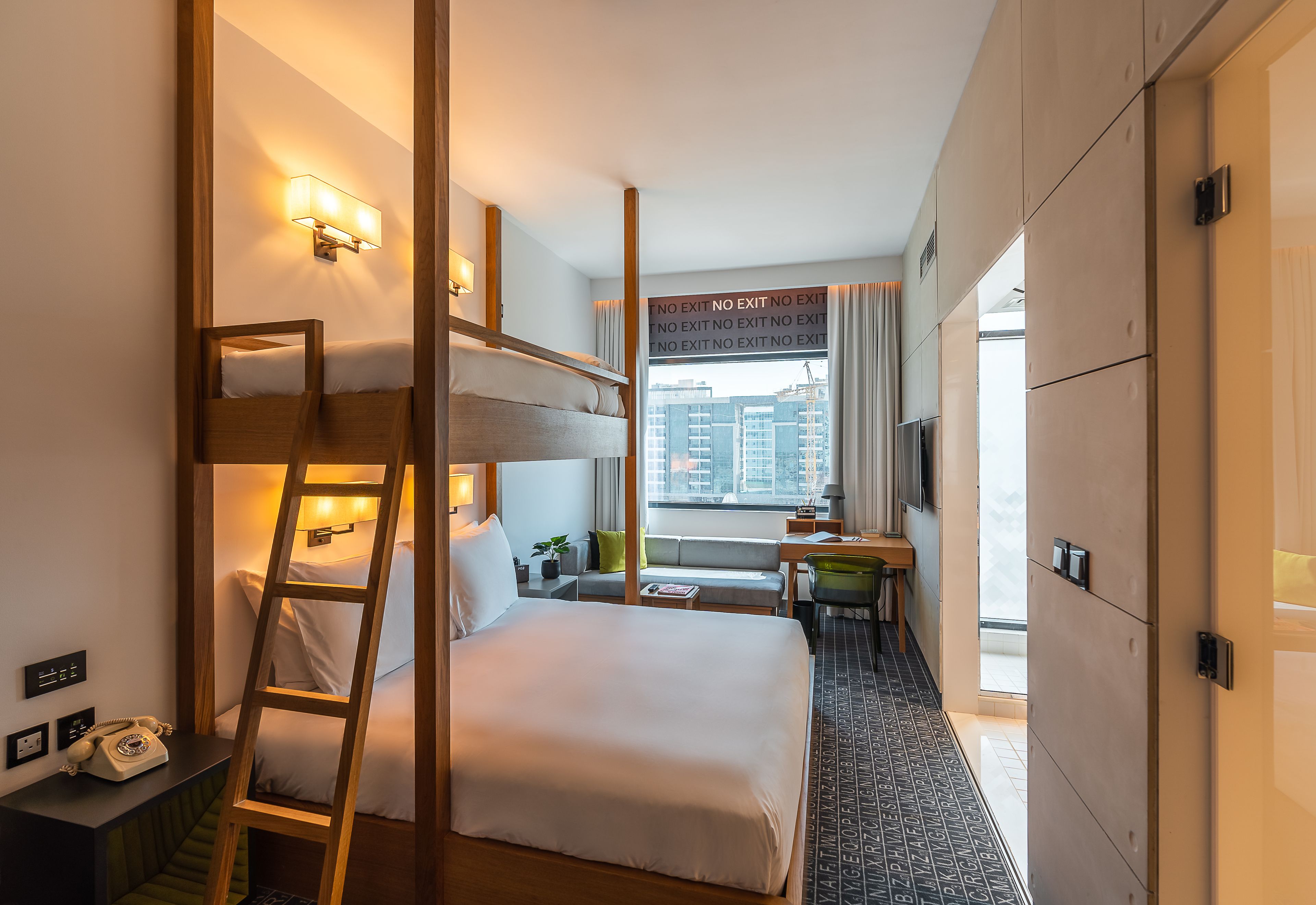 Habitación de hotel con literas, un escritorio con silla, una mesita, un sofá y un televisor.