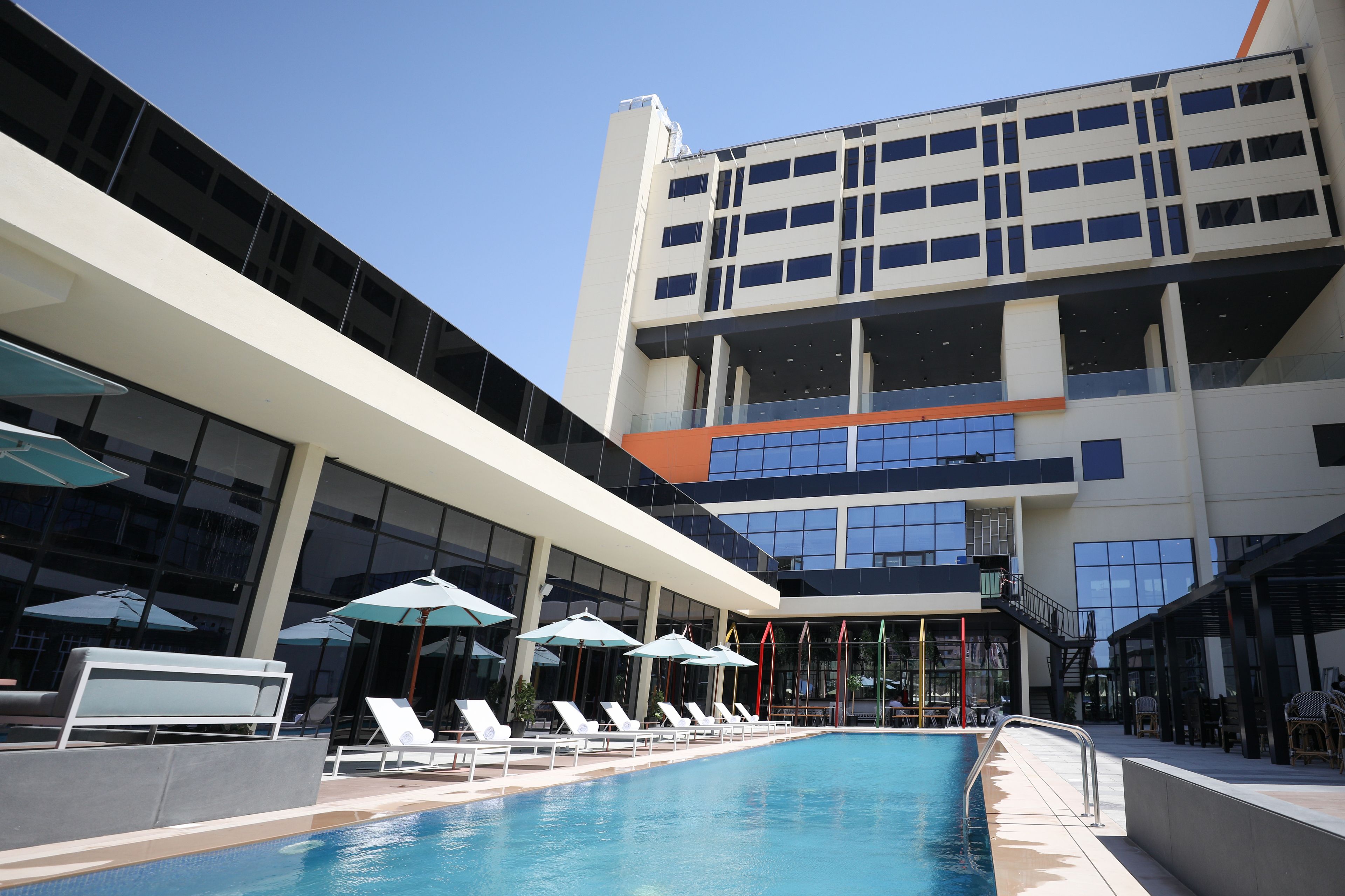 A modern hotel with a rooftop pool, lounge chairs, and umbrellas.