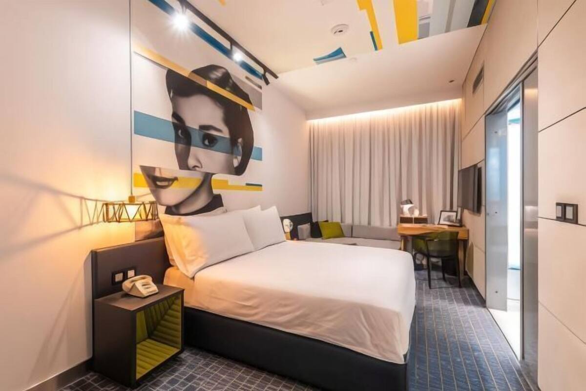 Ein modernes Hotelzimmer mit Bett, Nachttisch, Schreibtisch und großem Fenster.