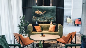 Un espace de détente moderne avec un canapé vert, des fauteuils orange et une table ronde en bois agrémentée d’une plante.