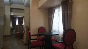 A dining area with a round table and four red chairs, a patterned sofa, and a window with curtains.