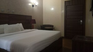 A hotel room with a large bed, a wooden headboard, a desk, and a wardrobe.