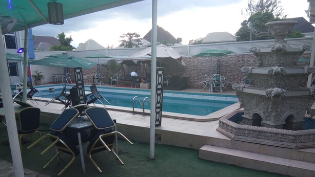 A pool area with lounge chairs and umbrellas, a stone fountain, and a covered seating area.