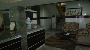 A lobby with a reception desk, a staircase, patterned sofas, and a framed picture on the wall.