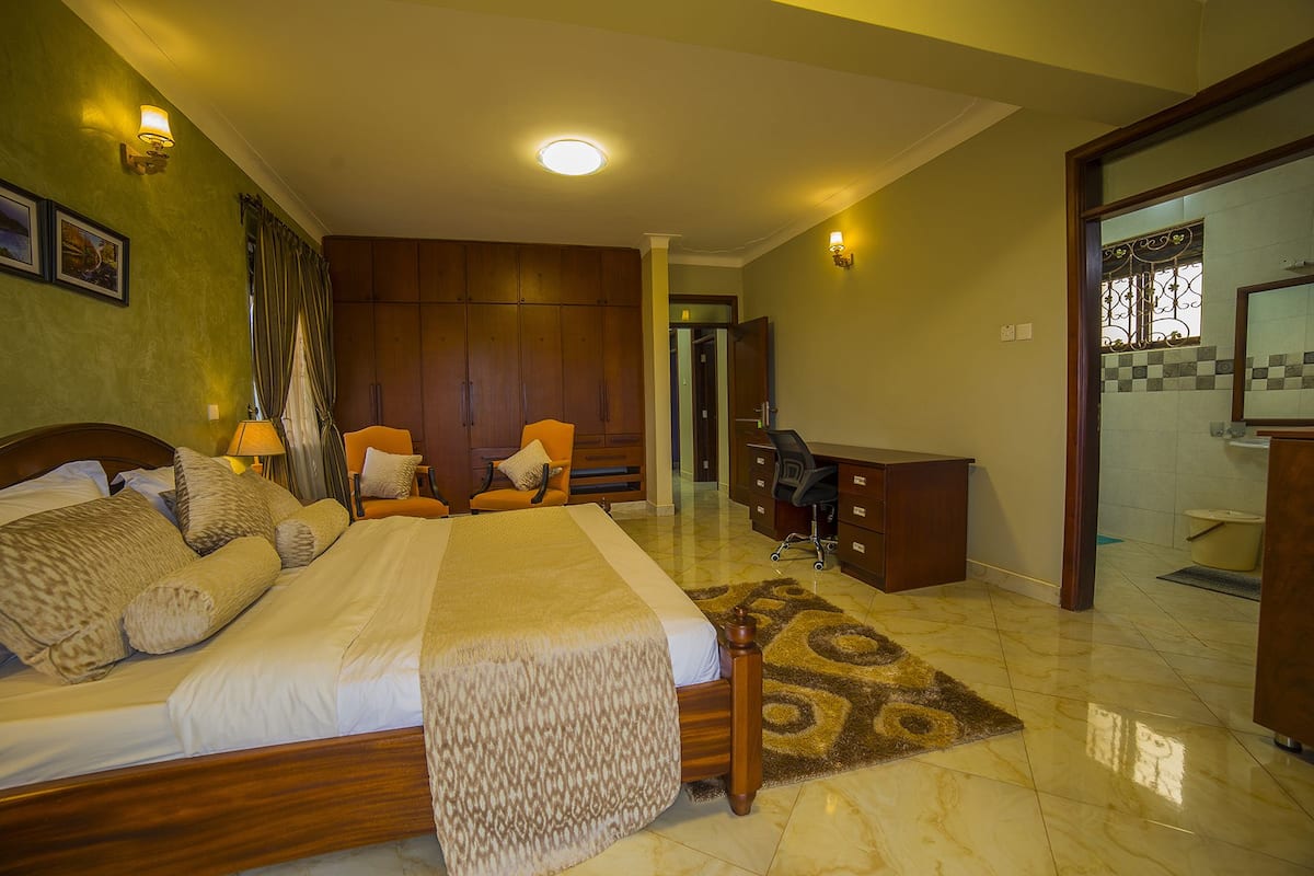 A bedroom with a large bed, two armchairs, a desk, and a bathroom visible through an open door.