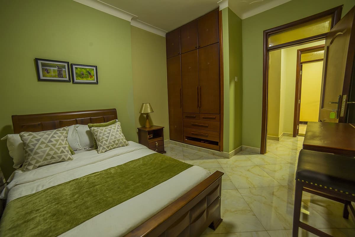 A bedroom with a bed, nightstand, lamp, wardrobe, and a desk.