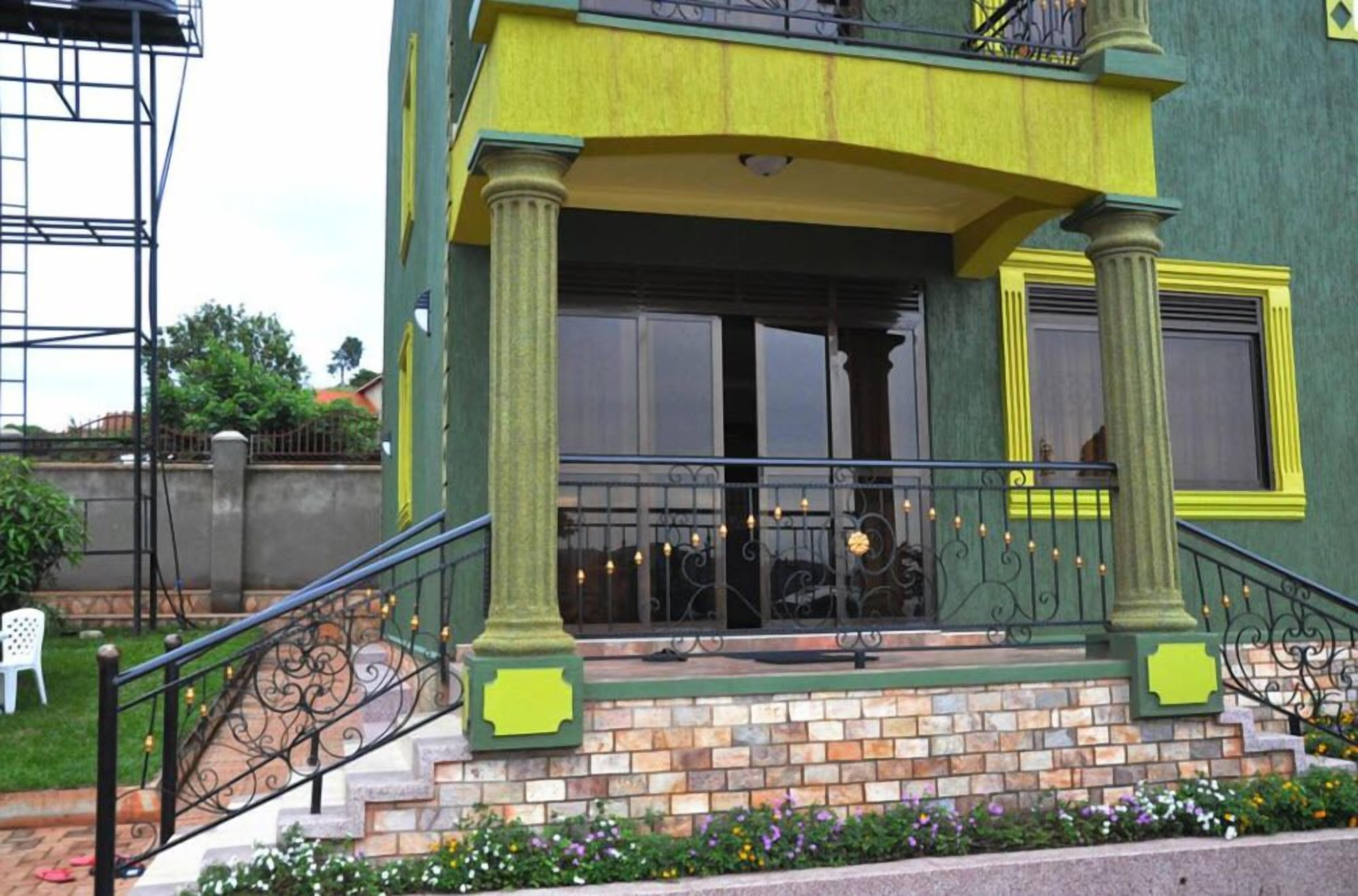 A two-story building with a green and yellow facade, a balcony with a wrought iron railing, and a brick base.