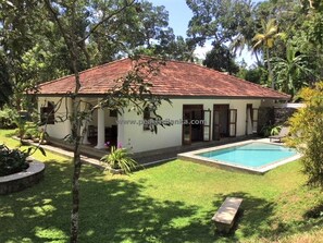 Surrounded by lush greenery, this charming property features a swimming pool and a cozy porch with a bench.