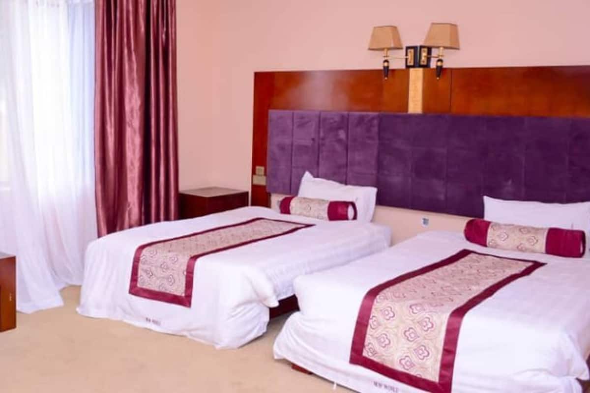 A hotel room with two beds, a sofa, a small table, and a nightstand.