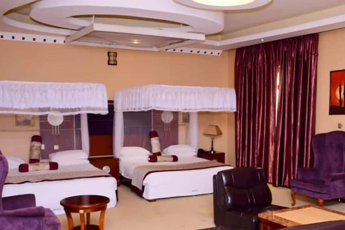 A hotel room with two beds, a desk, a chair, and a large window with curtains.