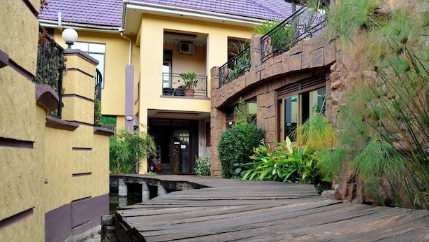 Un étroit sentier en bois mène à un bâtiment à la façade jaune et à l’arche d’entrée en pierre.