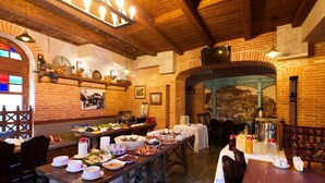 A restaurant with brick walls, wooden beams, and a long communal table set with various dishes and drinks. - Meidan Suites (Tbilisi)