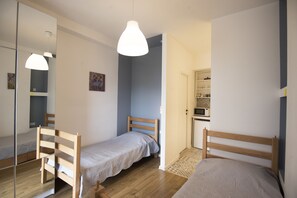 Une chambre avec deux lits en bois, une armoire, un miroir et une petite kitchenette.
