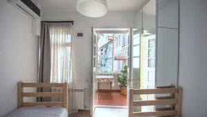 A room with two wooden beds, a radiator, a potted plant, and a view of a building through an open door. - Meidan Suites (Tbilisi)