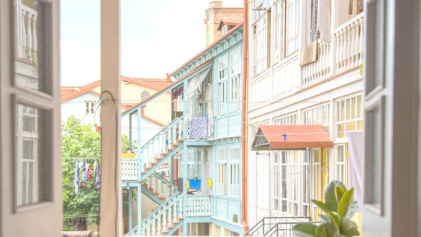 A balcony with a view of colorful buildings, a potted plant, and a table with a patterned tablecloth. - Meidan Suites (Tbilisi)