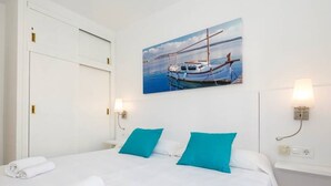 Et hotelværelse med en seng, to puder, et maleri af en båd og to vægmonterede lamper.