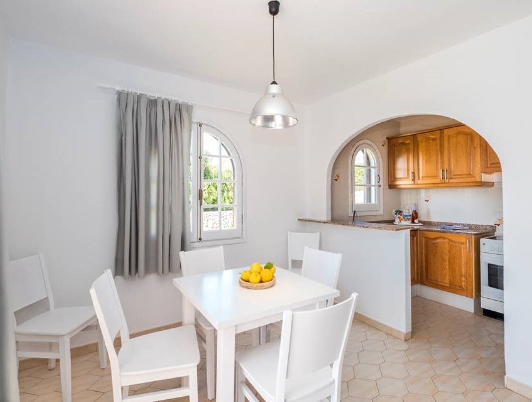 Une cuisine avec des meubles blancs, une table à manger avec des chaises et une fenêtre avec des rideaux.