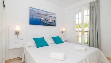 Ein Hotelzimmer mit Bett, zwei Kissen, einem Bootsgemälde, einem Deckenventilator und einem Vorhangfenster.