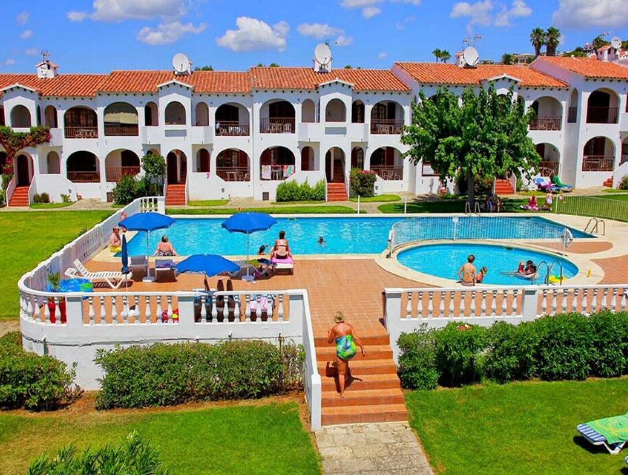 A resort with a swimming pool, outdoor seating, and a white building with arches.