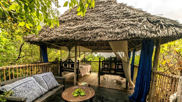A thatched-roof gazebo with a bench and table, surrounded by lush greenery. - Chole Mjini (Chole Island)