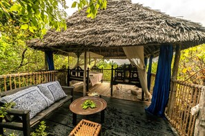 A thatched-roof gazebo with a bench and table, surrounded by lush greenery. - Chole Mjini (Chole Island)