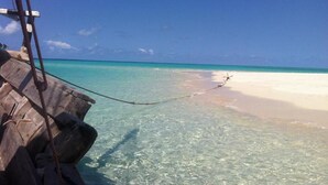 A wooden boat docked at a beach with clear turquoise water and a sandy shore. - Chole Mjini (Chole Island)