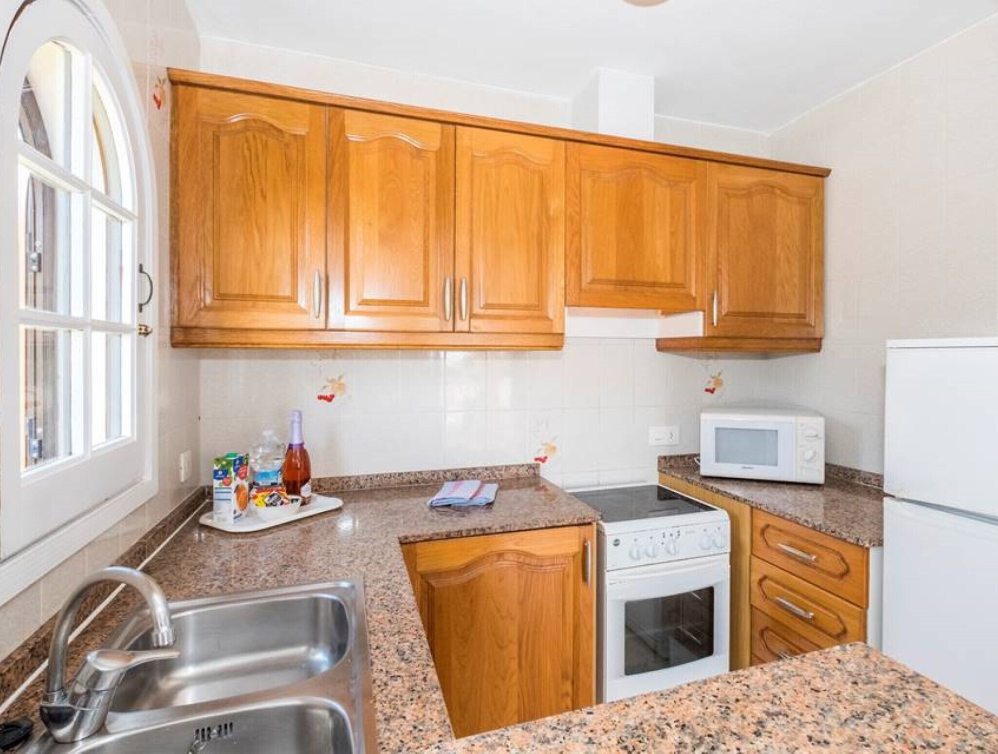 A kitchen with wooden cabinets, a stainless steel sink, a microwave, and an oven.
