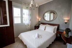 A neatly made bed with white linens, a round mirror on the wall, and a nightstand with a vase of flowers.